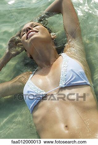 Young woman in bikini lying in shallow water on beach View Large Photo Image Stock Image - Young woman in bikini lying in shallow water on beach. Fotosearch