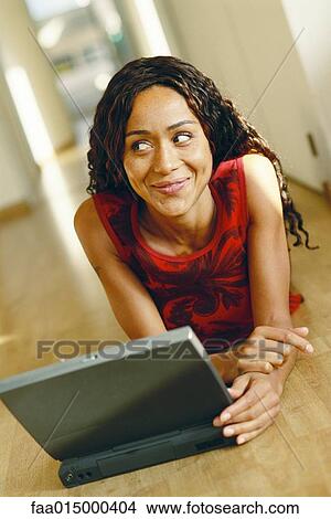 Young woman lying on ground with laptop, smiling and looking away View Large Photo Image Picture - Young woman lying on ground with laptop, smiling and looking away. Fotosearch