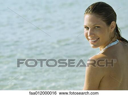 Stock Photograph - Young woman on beach, looking over shoulder at camera. Fotosearch