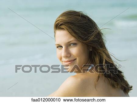 Stock Image - Young woman on beach, smiling over shoulder at camera. Fotosearch