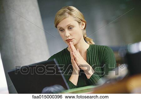 Young woman using laptop, hands clasped in front of chin View Large Photo Image Stock Photograph - Young woman using laptop, hands clasped in front of chin. Fotosearch