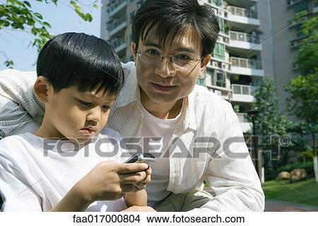 Picture - Boy and father, boy using cell phone. Fotosearch