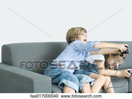 Stock Image - Boy and girl playing video game, holding out joysticks on sofa. Fotosearch