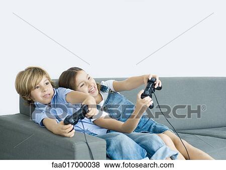 Stock Photo - Boy and girl playing video game, holding out joysticks on sofa. Fotosearch