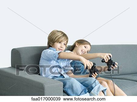 Stock Photo - Boy and girl playing video game, holding out joysticks on sofa. Fotosearch