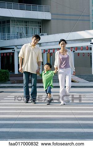 Stock Image - Boy crossing crosswalk, hand in hand with parents, full length. Fotosearch