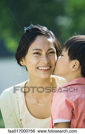 Stock Photograph - Boy kissing mother on cheek, woman smiling at camera, close-up. Fotosearch