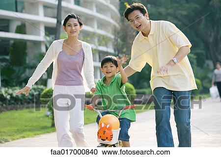 Stock Image - Boy riding bicycle, parents on either side, waving at camera. Fotosearch