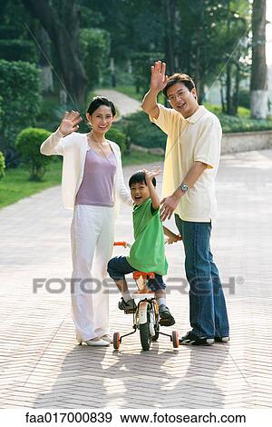 Boy riding bicycle, parents on either side, waving at camera View Large Photo Image Stock Photo - Boy riding bicycle, parents on either side, waving at camera. Fotosearch
