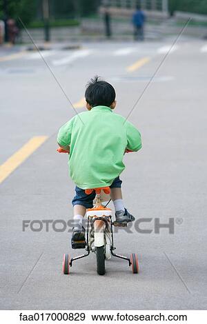 Stock Photo - Boy riding bicycle with training wheels, rear view. Fotosearch