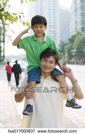 Stock Photo - Boy riding on father's shoulders, saluting camera. Fotosearch