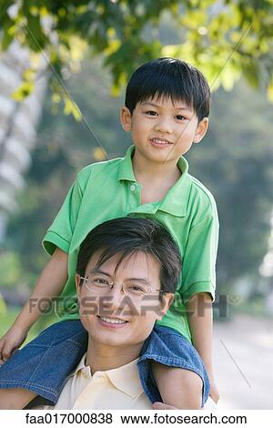 Boy sitting on father's shoulders, smiling at camera View Large Photo Image Stock Photo - Boy sitting on father's shoulders, smiling at camera. Fotosearch