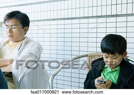 Boy using cell phone while father sits with eyes closed View Large Photo Image Stock Image - Boy using cell phone while father sits with eyes closed. Fotosearch