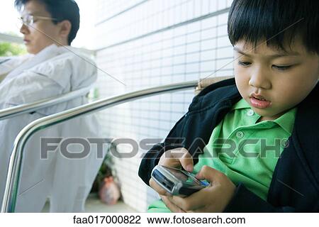 Stock Image - Boy using cell phone while father sits with eyes closed. Fotosearch