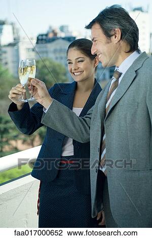 Stock Image - Business partners clinking glasses of champagne, skyline in background. Fotosearch