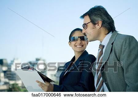 Stock Photograph - Business partners looking at documents, skyline in background. Fotosearch