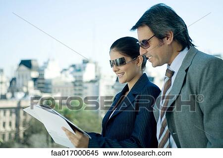 Stock Photography - Business partners looking at documents, skyline in background. Fotosearch
