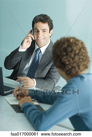 Stock Image - Businessman and casually dressed young man having meeting, man using cell phone. Fotosearch