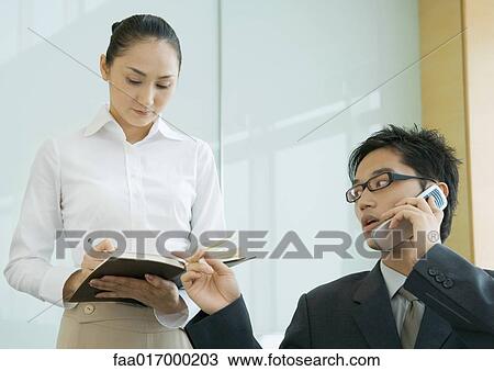 Stock Image - Businessman and female assistant, man using phone and gesturing to agenda. Fotosearch