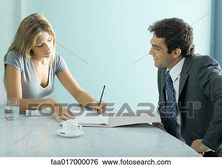 Stock Photograph - Businessman and female colleague sitting at table, woman taking notes. Fotosearch