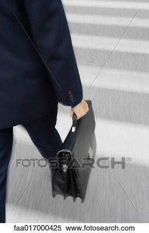 Stock Photography - Businessman carrying briefcase across crosswalk, low section. Fotosearch