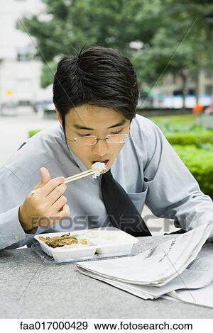 Businessman eating lunch with chopsticks and reading newspaper View Large Photo Image Stock Photo - Businessman eating lunch with chopsticks and reading newspaper. Fotosearch