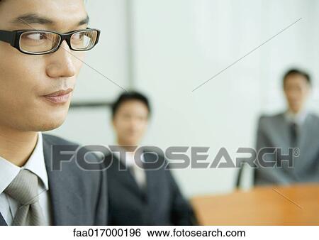 Businessman glancing away, colleagues sitting in blurred background View Large Photo Image Stock Photograph - Businessman glancing away, colleagues sitting in blurred background. Fotosearch