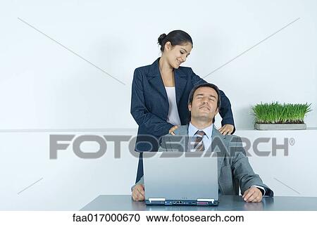 Stock Image - Businessman having shoulder massage from female colleague. Fotosearch