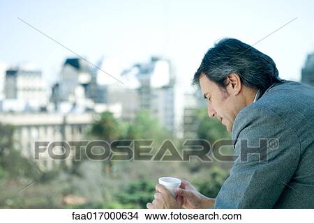 Businessman holding cup, city in background View Large Photo Image Picture - Businessman holding cup, city in background. Fotosearch