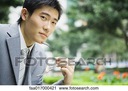 Stock Image - Businessman holding glasses, looking at camera, portrait. Fotosearch