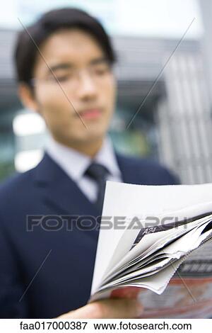 Stock Photo - Businessman holding newspaper, focus on newspaper in foreground. Fotosearch