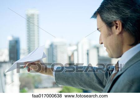 Stock Photo - Businessman holding out paper airplane, skyline in background. Fotosearch