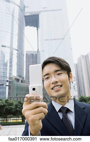 Stock Image - Businessman holding up cell phone, smiling. Fotosearch