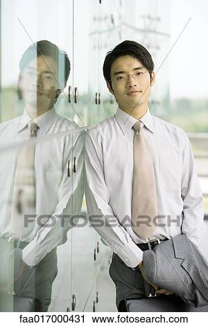 Stock Image - Businessman leaning against glass wall, portrait. Fotosearch