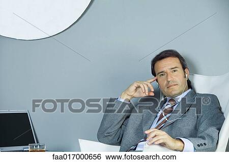 Businessman listening to earphones, looking at camera View Large Photo Image Stock Photograph - Businessman listening to earphones, looking at camera. Fotosearch