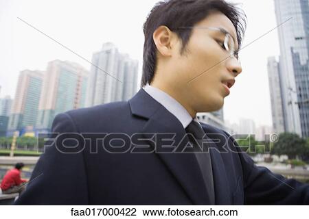 Stock Image - Businessman looking down, high rises in background. Fotosearch