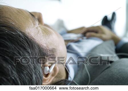 Picture - Businessman lying down, listening to earphones. Fotosearch