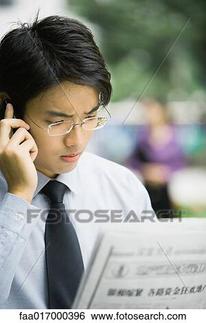 Businessman reading newspaper and using cell phone, frowning View Large Photo Image Stock Photograph - Businessman reading newspaper and using cell phone, frowning. Fotosearch