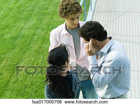 Stock Photograph - Businessman sharing earphones with teenage couple. Fotosearch