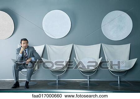 Businessman sitting at end of row of chairs, holding laptop on lap View Large Photo Image Stock Image - Businessman sitting at end of row of chairs, holding laptop on lap. Fotosearch