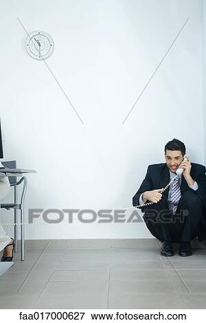 Stock Photo - Businessman sitting in corner, talking on telephone. Fotosearch