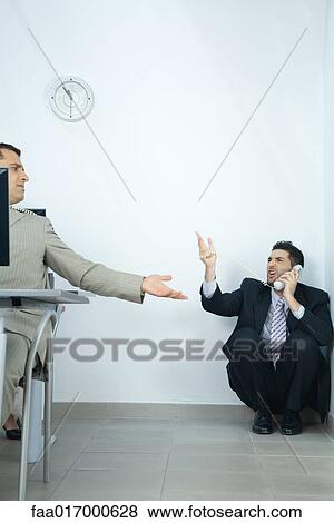 Stock Photo - Businessman sitting in corner, using telephone, arguing with colleague in foreground. Fotosearch