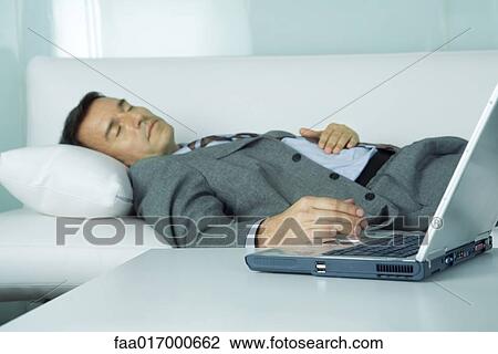 Businessman sleeping on sofa, hand resting on laptop View Large Photo Image Stock Image - Businessman sleeping on sofa, hand resting on laptop. Fotosearch