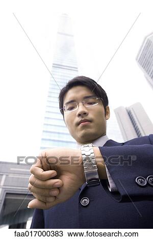 Businessman standing checking time on wristwatch, skyscraper in background View Large Photo Image Stock Image - Businessman standing checking time on wristwatch, skyscraper in background. Fotosearch