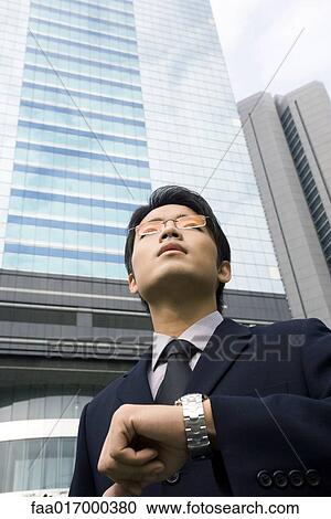 Businessman standing holding up wrist with watch, skyscraper in background View Large Photo Image Stock Image - Businessman standing holding up wrist with watch, skyscraper in background. Fotosearch
