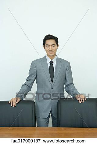 Businessman standing in conference room with hands on backs of chairs, portrait View Large Photo Image Stock Photo - Businessman standing in conference room with hands on backs of chairs, portrait. Fotosearch
