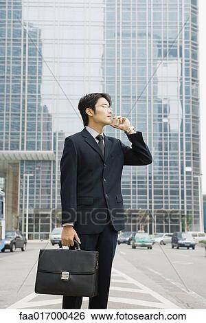Businessman standing on median of street, using cell phone View Large Photo Image Stock Photograph - Businessman standing on median of street, using cell phone. Fotosearch