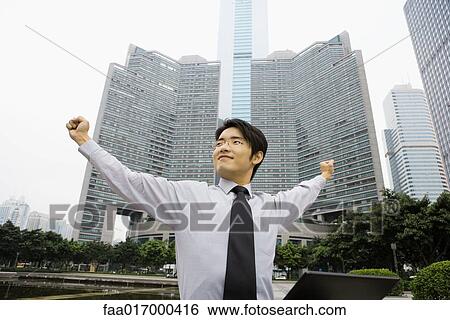 Stock Photograph - Businessman standing with arms out, skyscraper in background, low angle view. Fotosearch