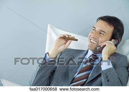 Stock Photo - Businessman using cell phone and smoking cigar. Fotosearch