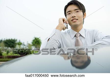 Stock Image - Businessman using cell phone, leaning against roof of car. Fotosearch